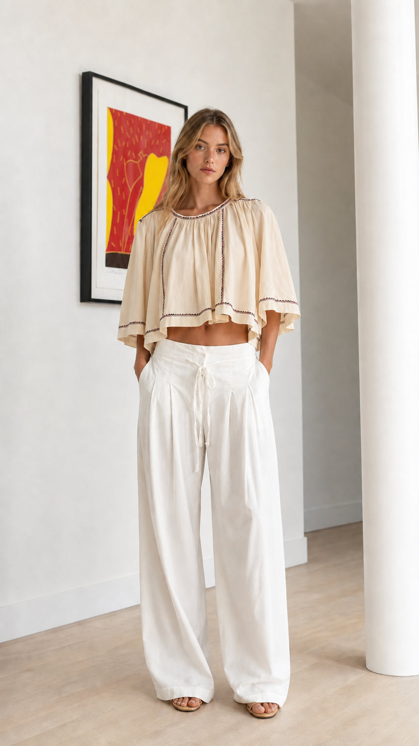 Front view of beige oatmeal embroidered cropped swing top with white trousers