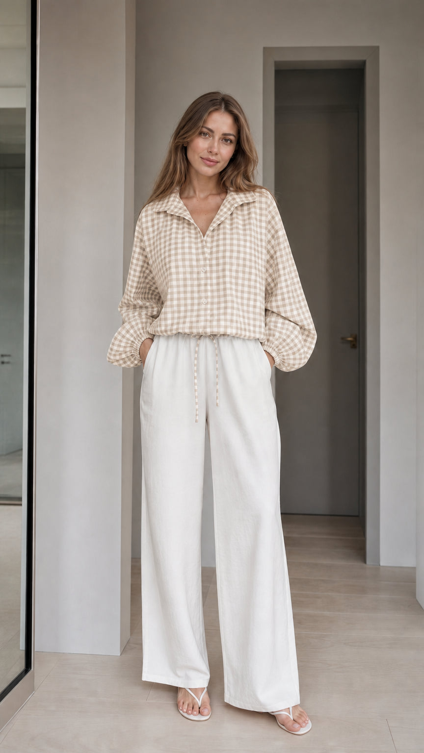 Woman wearing beige gingham check blouse and white wide-leg trousers, front view