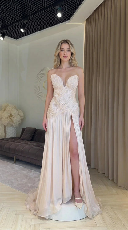 Front view of model wearing champagne strapless pleated evening dress with high slit