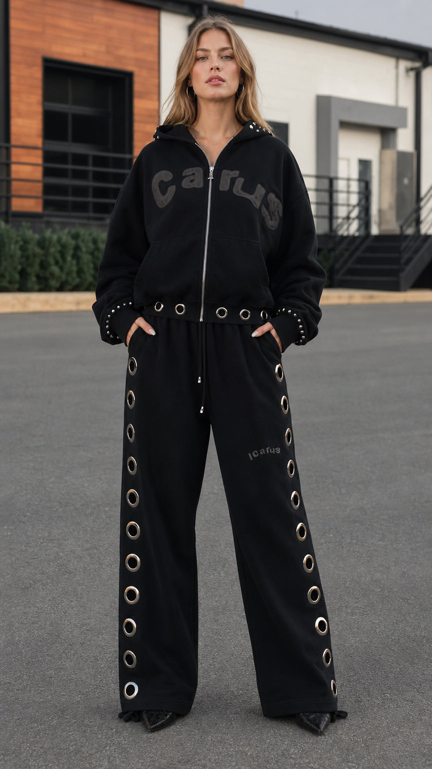 Full front view of model wearing black zip-up hoodie and grommet wide-leg sweatpants tracksuit set