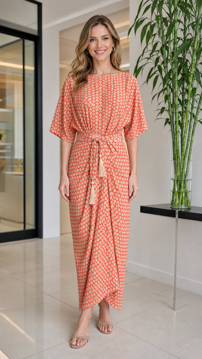 Front view of woman wearing orange geometric print maxi dress with tassel belt