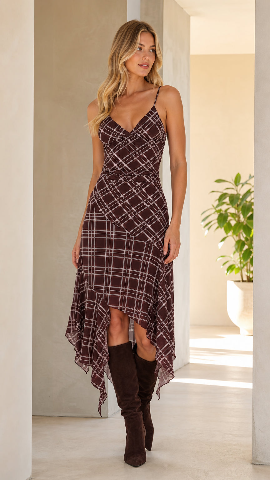 Front view of woman wearing brown plaid asymmetrical cami midi dress with boots