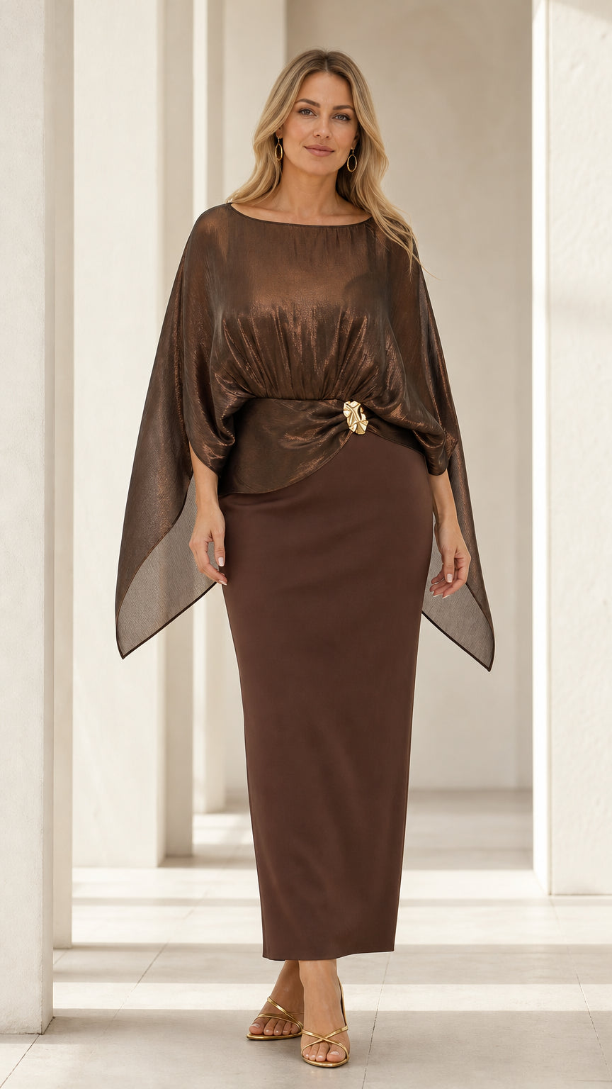 Front view of woman wearing metallic brown shimmer capelet maxi dress with gold waist brooch