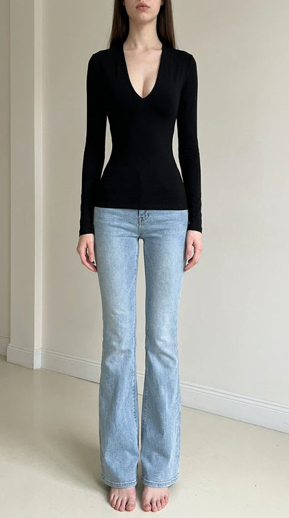 Front view of woman wearing black deep v-neck long sleeve top with light wash jeans