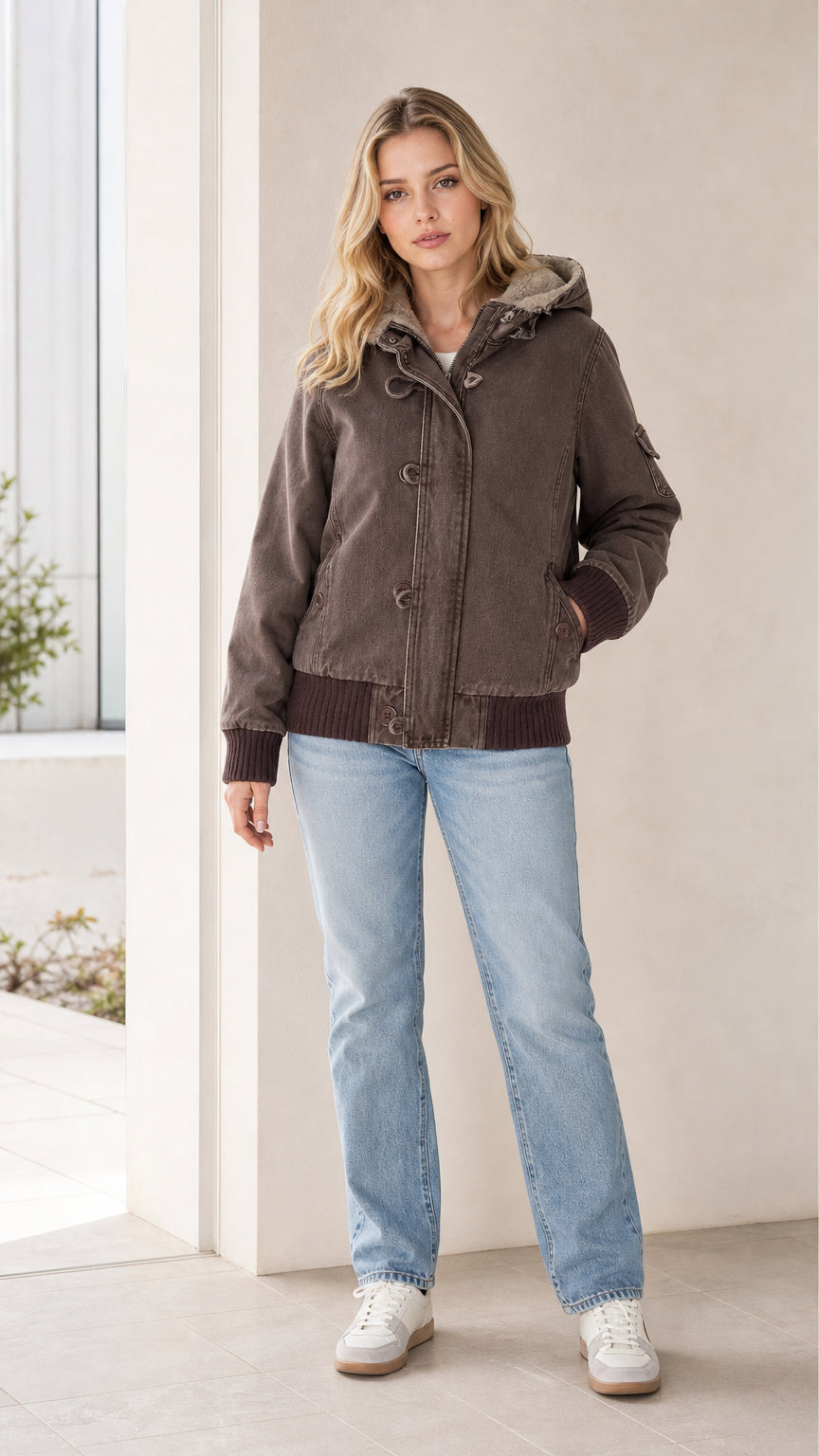 Front full view of a woman wearing a brown canvas sherpa hooded bomber jacket with light-wash jeans