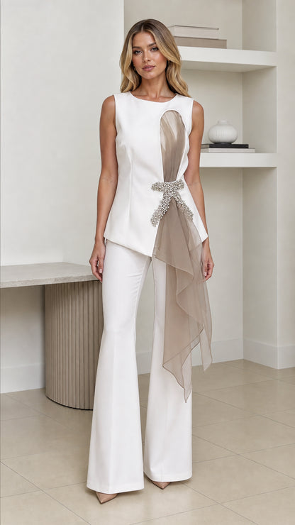 Front view of woman wearing white crystal embellished asymmetric top with white flared trousers