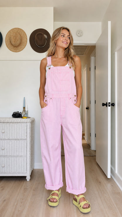 Model wearing pink wide-leg bib overalls with adjustable straps and rolled hems