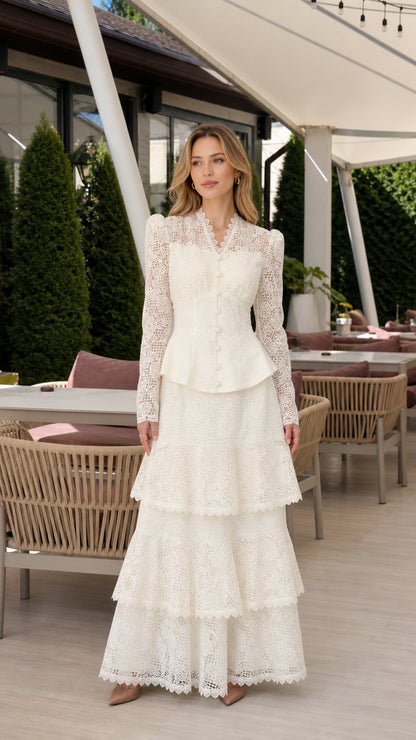 Front full view of woman wearing ivory long-sleeve lace peplum tiered maxi dress in outdoor terrace