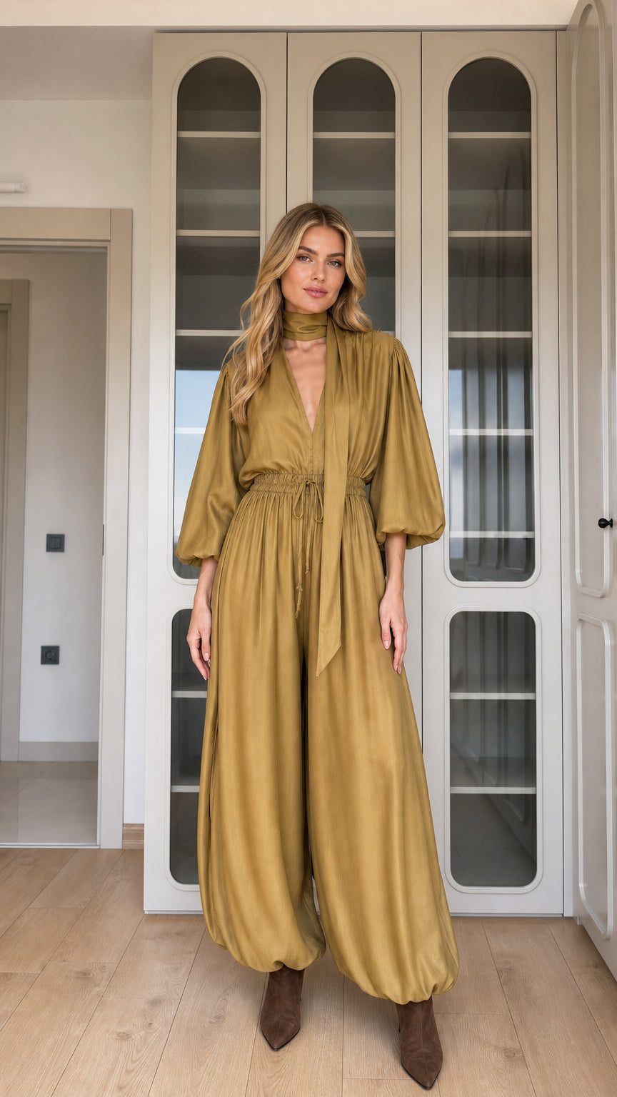 Front view of woman wearing mustard draped balloon sleeve jumpsuit with neck scarf
