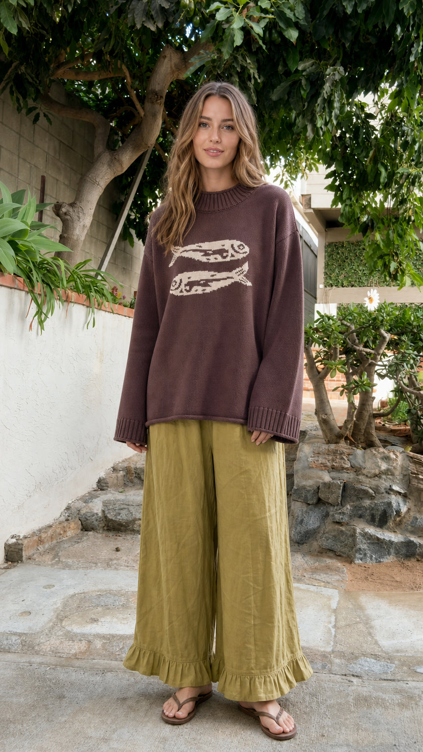 Front view of model wearing Brown oversized fish motif knit crewneck sweater with wide-leg pants