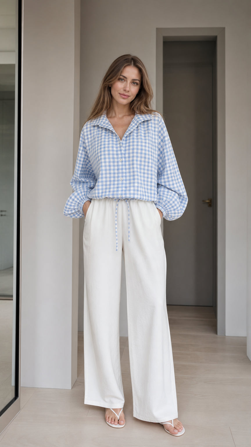 Woman wearing light blue gingham check blouse and white wide-leg trousers, front view