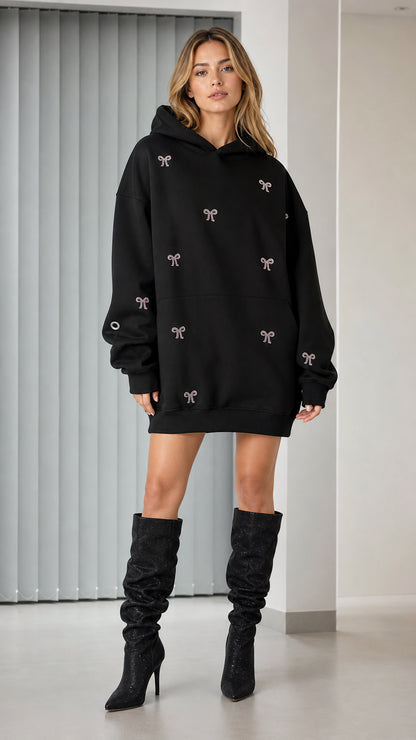 Front view of model wearing black rhinestone bow oversized hoodie dress with knee-high boots