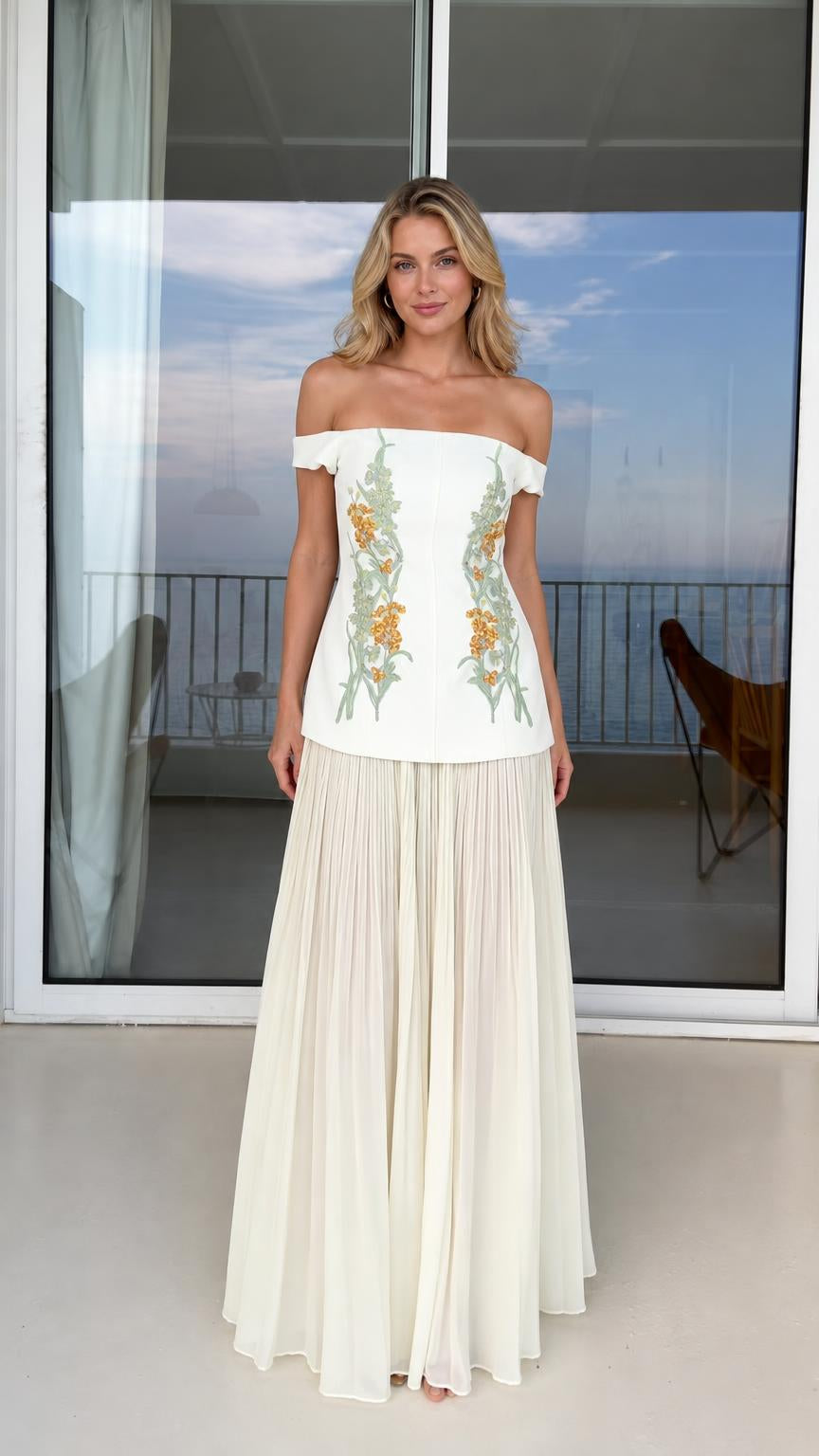 Front view of model wearing white off-shoulder floral embroidered top and pleated maxi skirt