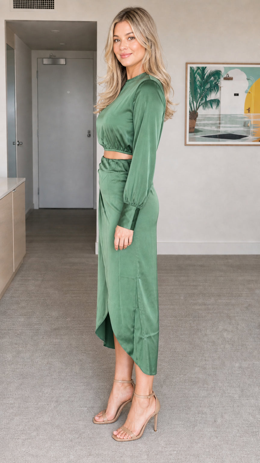 Side angle view of model wearing sage green satin long sleeve crop top and midi skirt