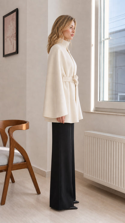 Side profile view of cream stand-collar cape coat showing draped sleeve design