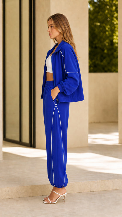Side view of model wearing royal blue two-piece tracksuit with white piping along sleeves and pants