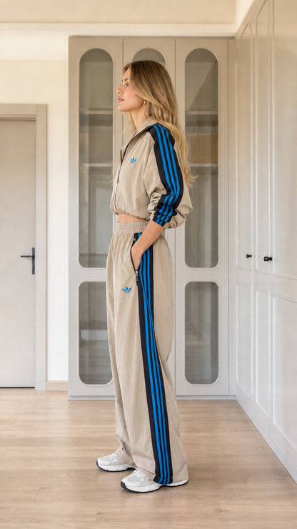 Side view of model wearing khaki tan two-piece track pants set with contrast side stripes