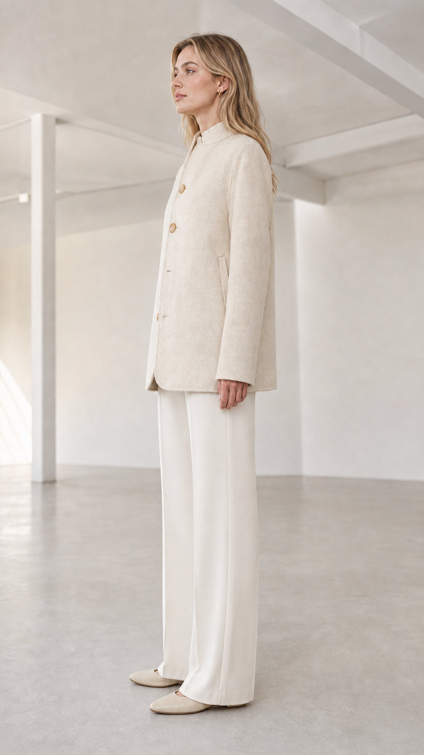Three-quarter side view of model in cream stand collar tailored coat