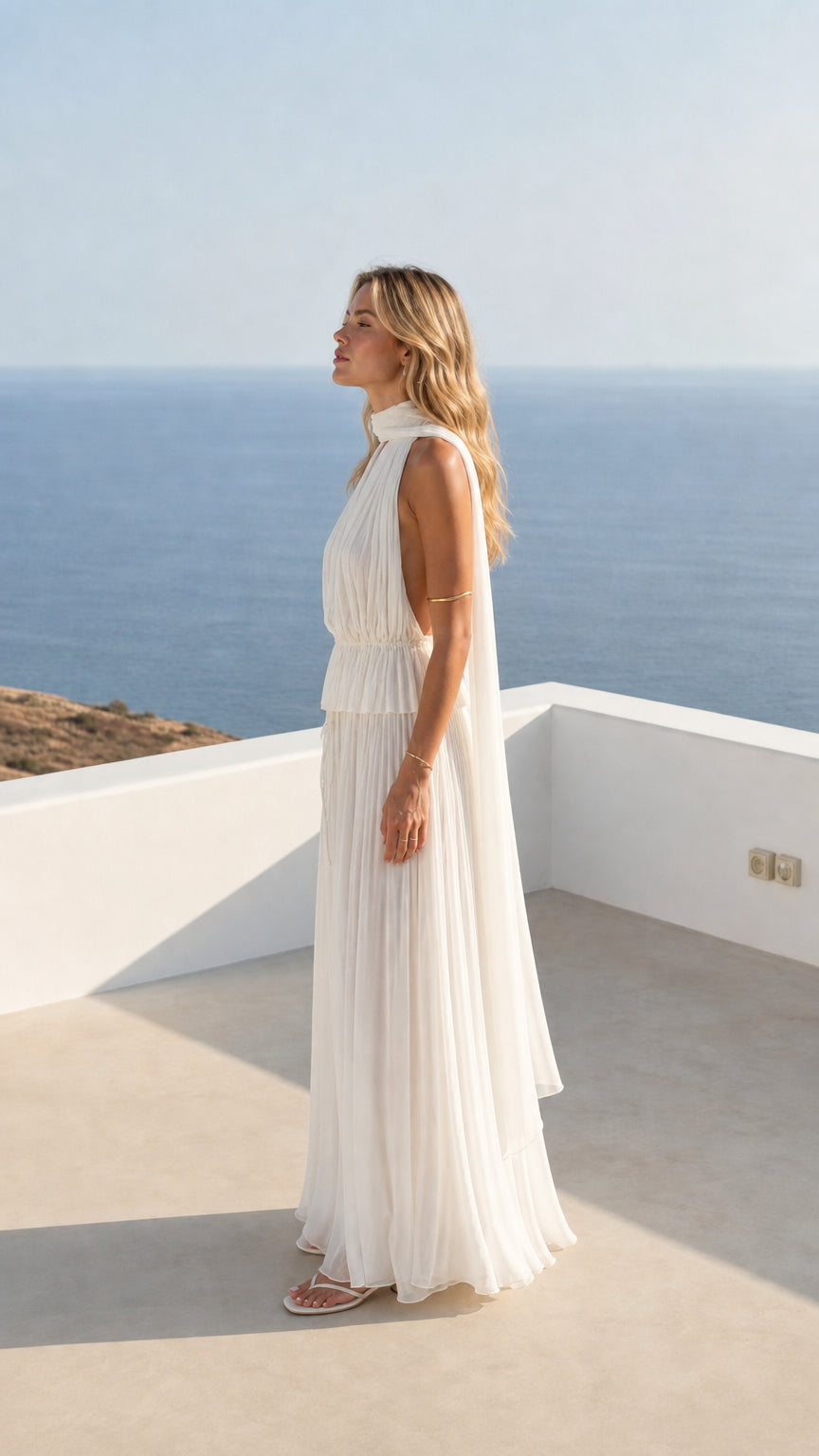 Side profile of woman in flowing white pleated maxi dress