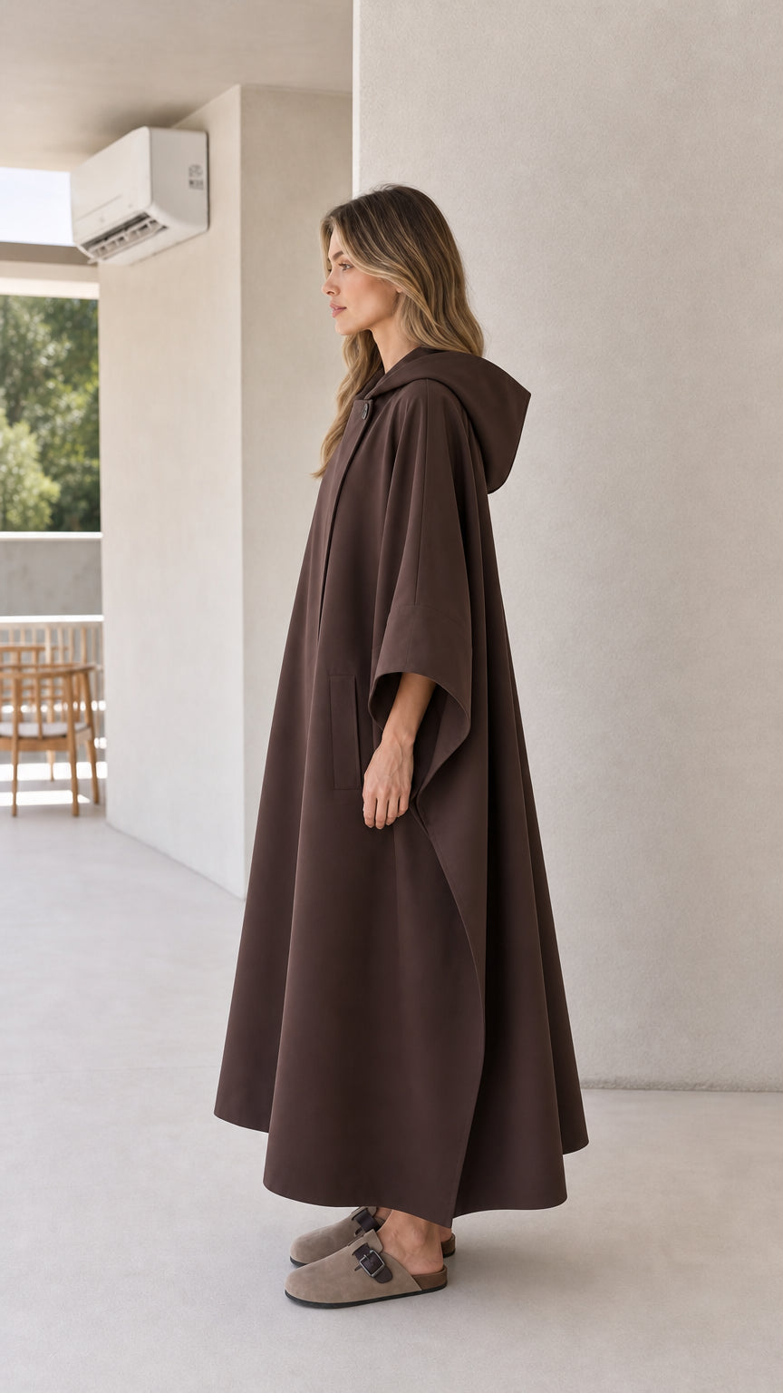 Side profile of model wearing brown flowing cape cloak with hood