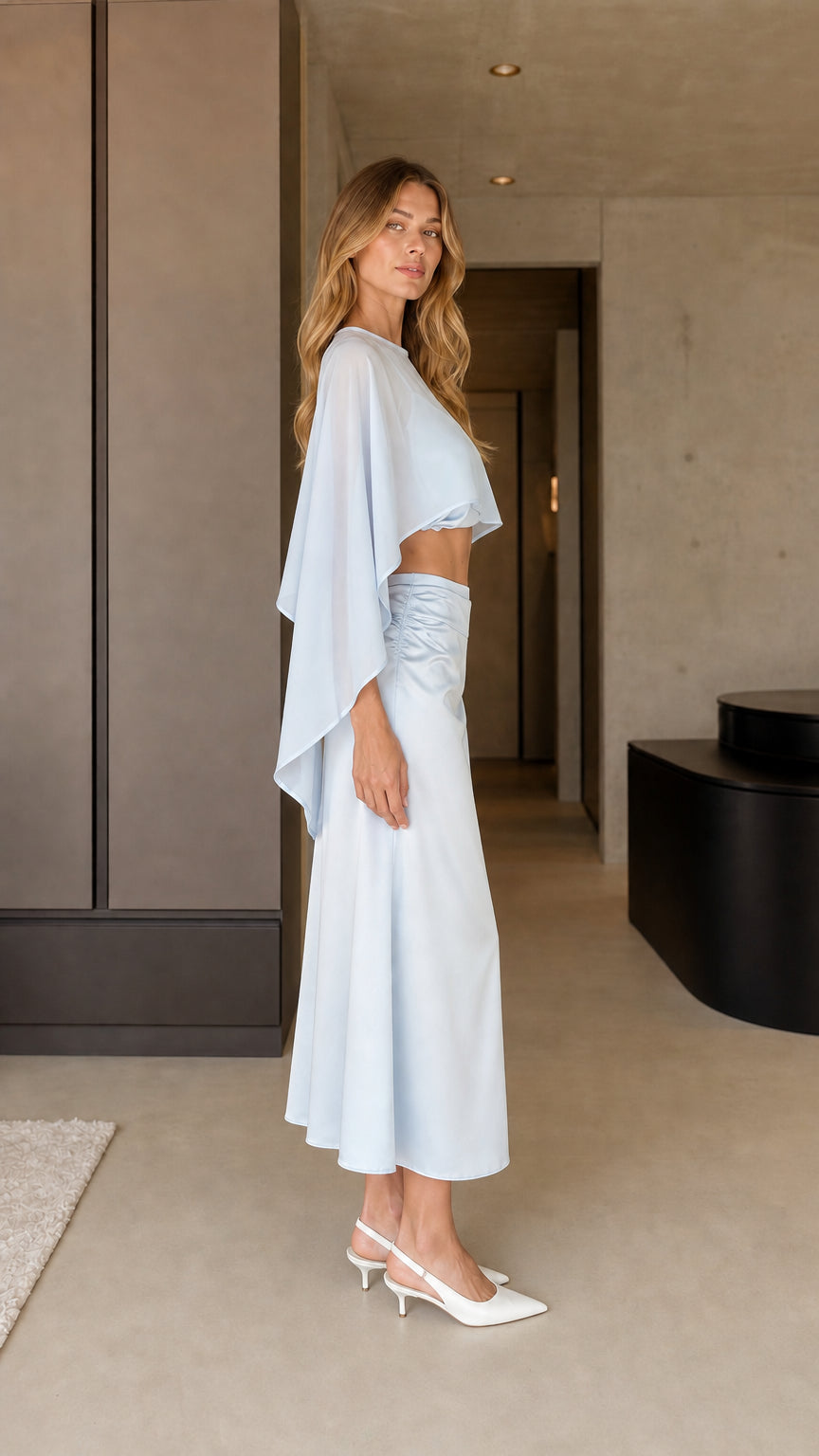Side view of model in light blue cape top and midi skirt
