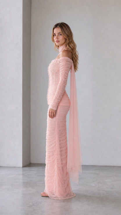 Blush pink fitted evening gown shown from the side with flowing tulle overlay