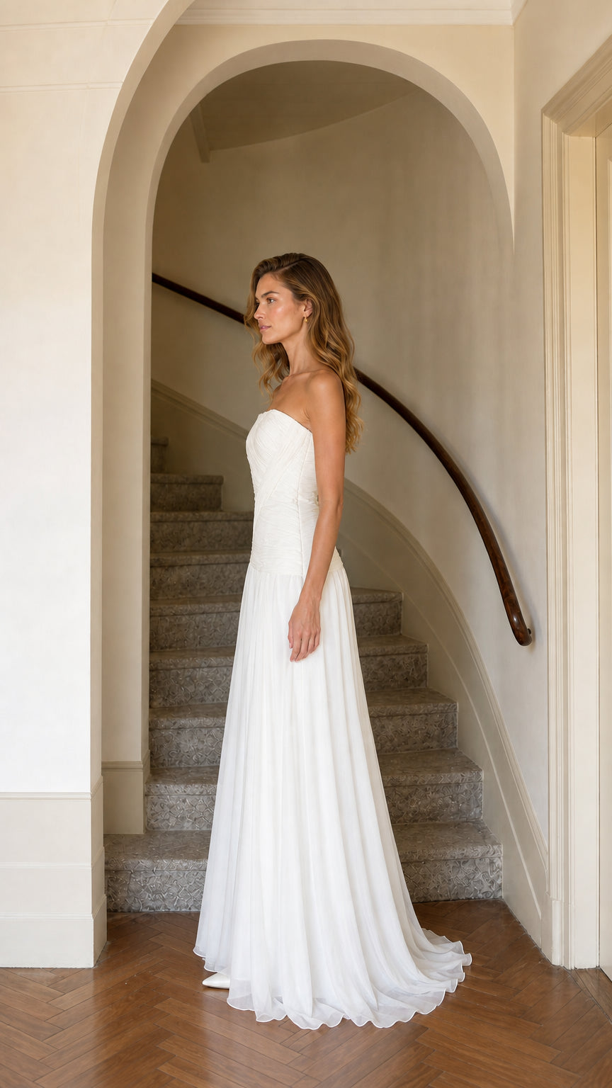 Side profile view of strapless white pleated maxi evening gown