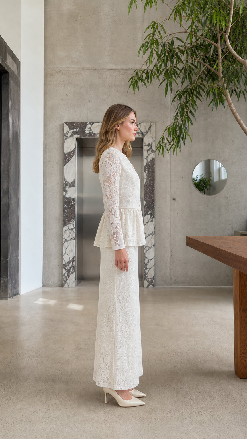 Side profile view of model wearing the Cream long-sleeve lace peplum top and maxi skirt set