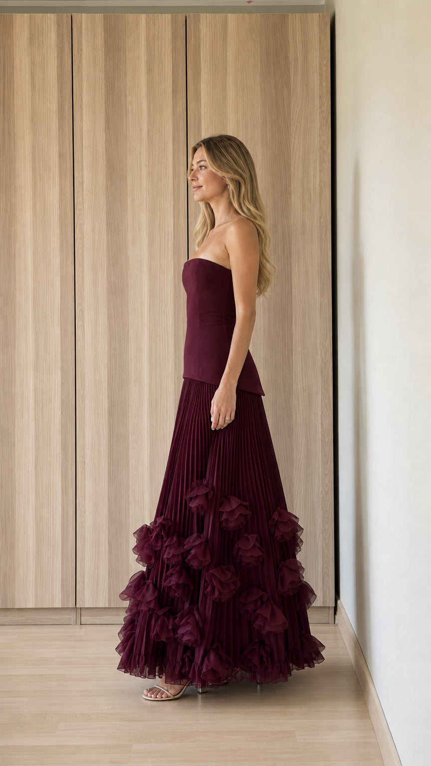Side profile view of burgundy strapless pleated evening dress