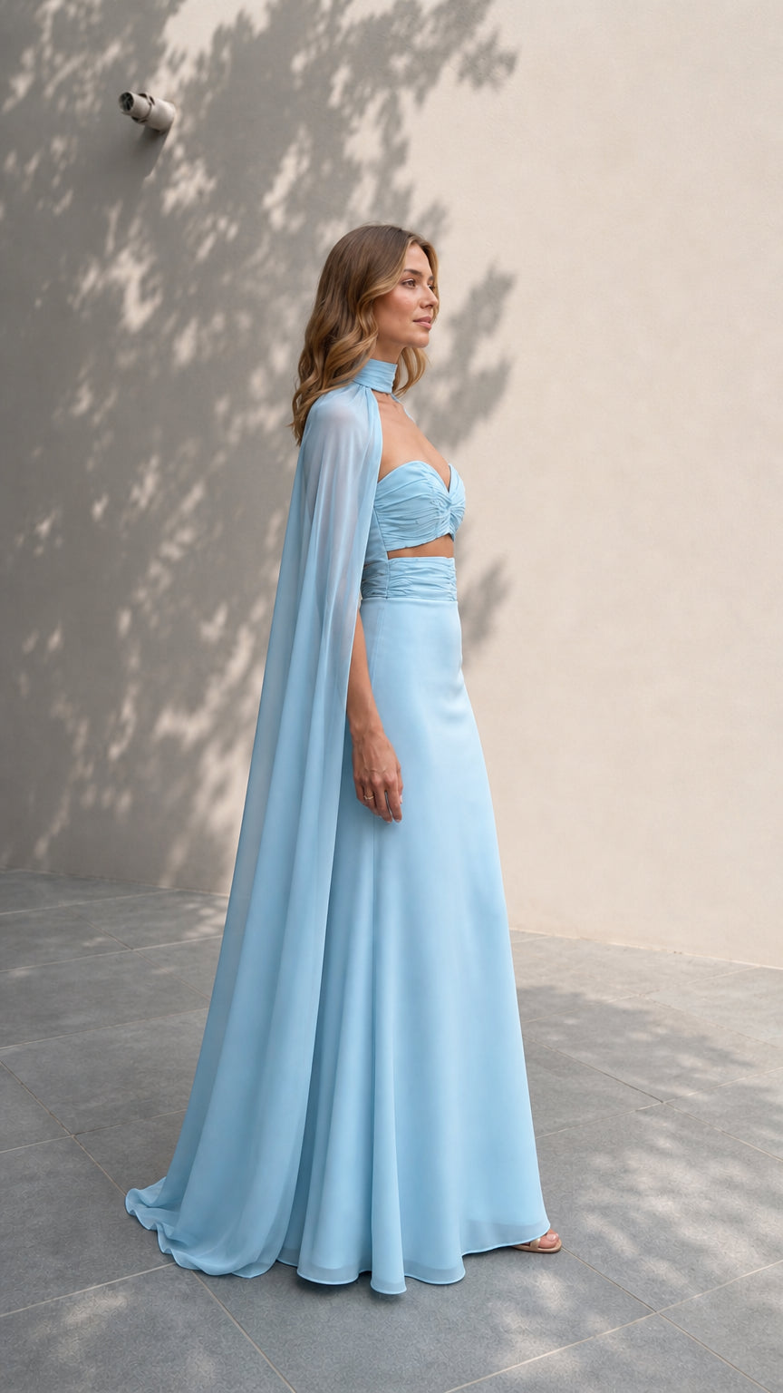 Side profile of model in light blue two-piece gown with dramatic cape