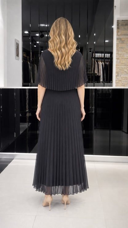 Model wearing black pleated cape overlay maxi dress, back view