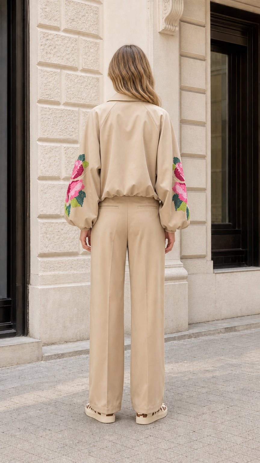 Back view of model wearing beige two-piece suit set with embroidered sleeves and wide-leg pants