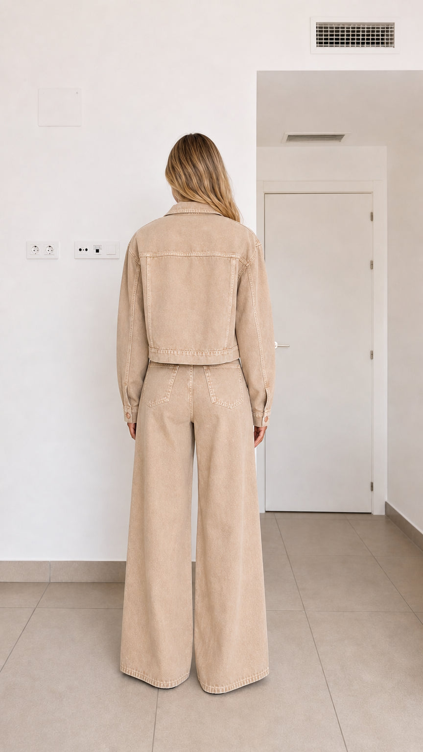 Back view of woman wearing beige cropped denim jacket and matching wide-leg trousers