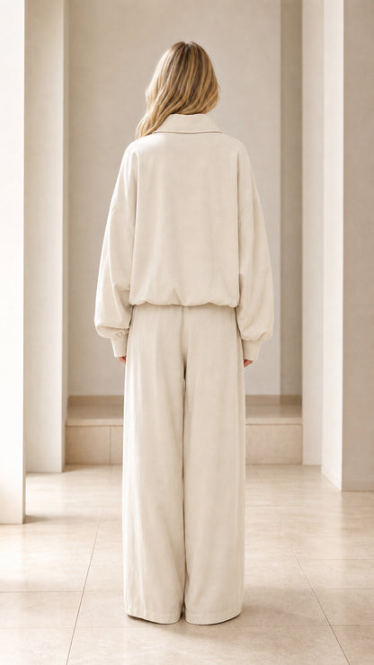 Back view of woman wearing cream relaxed zip jacket and flowing wide-leg pants