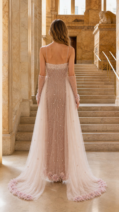 Blush embellished evening gown shown from the back with flowing outer layers