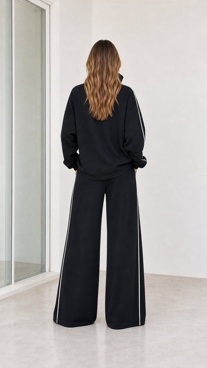 Back view of model wearing black wide leg lounge set with contrast white piping