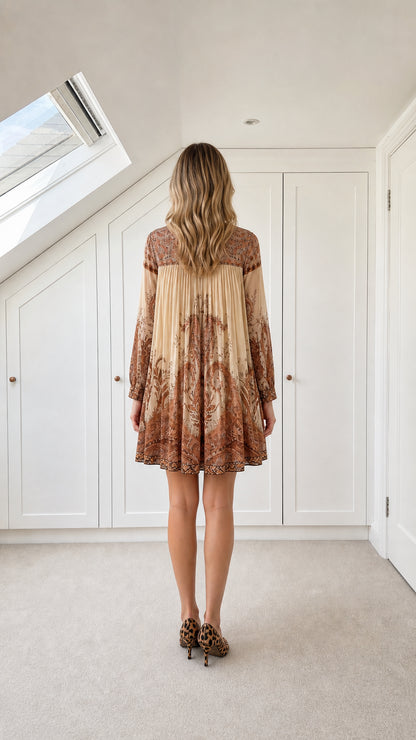 Back view of model wearing the beige pleated long sleeve paisley mini dress