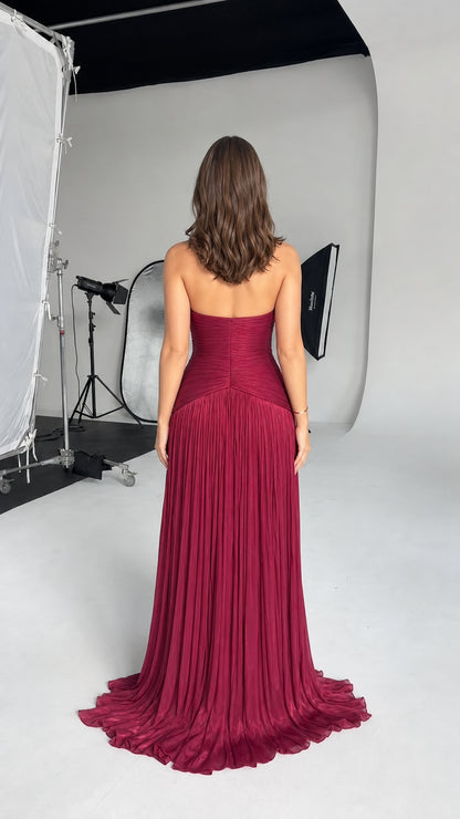 Back view of model wearing burgundy backless pleated evening dress with train