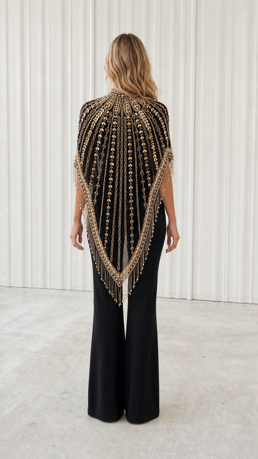 Back view of model wearing black embellished fringe capelet with deep V drape