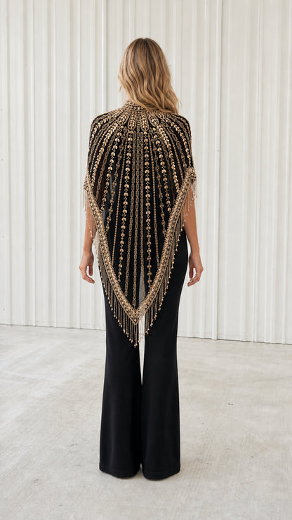 Back view of model wearing black embellished fringe capelet with deep V drape