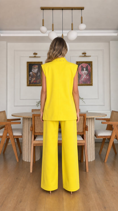 Back view of model showing clean cut of yellow sleeveless longline vest and wide trousers