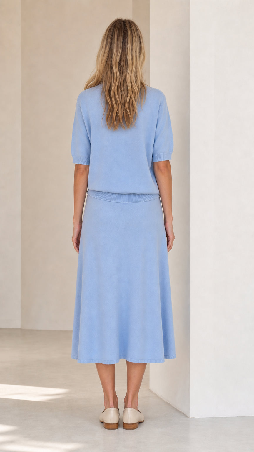 Back view of woman wearing light blue knit sweater and skirt set