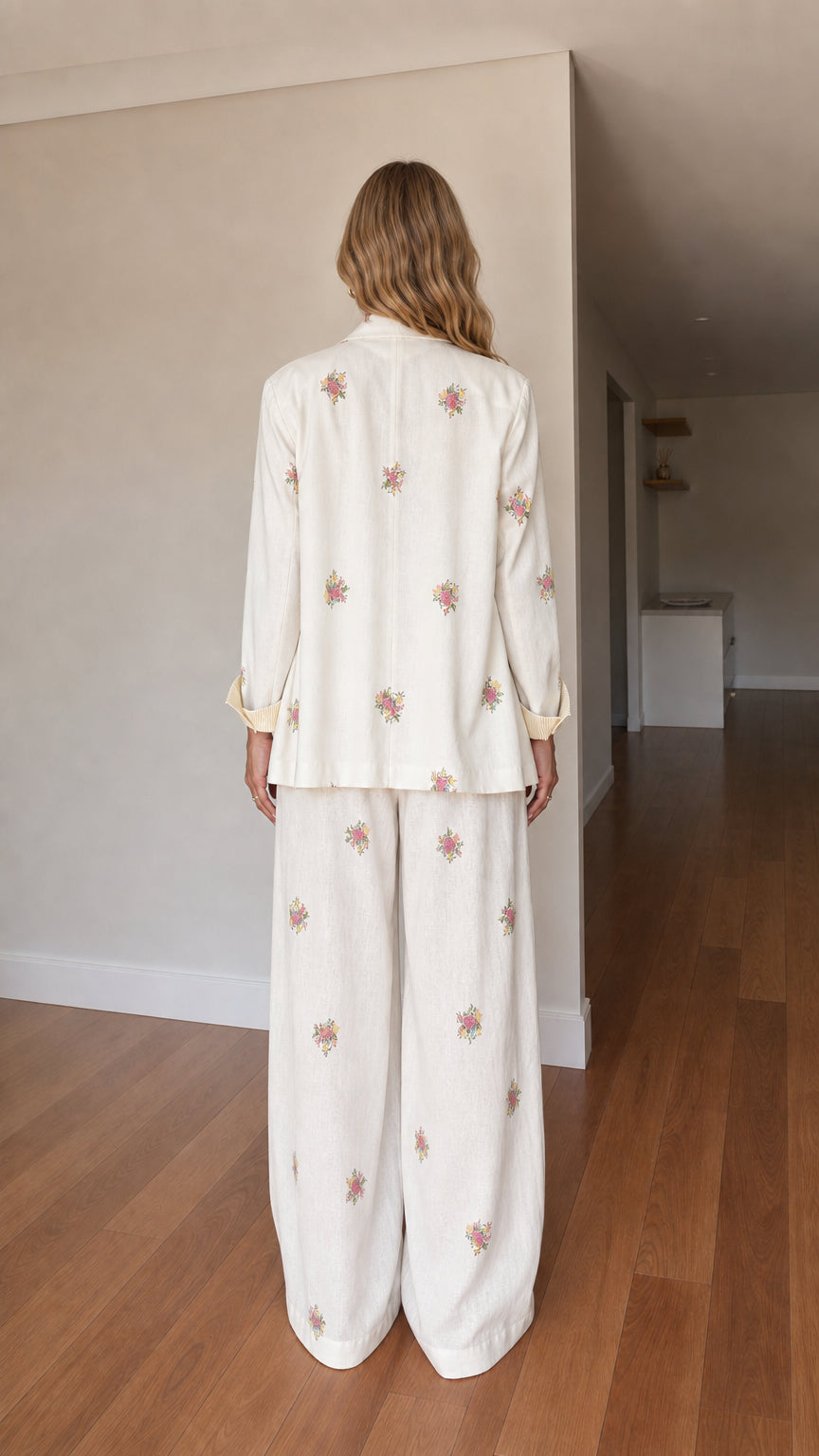 Back view of woman wearing cream floral embroidered tailored blazer and wide-leg trousers