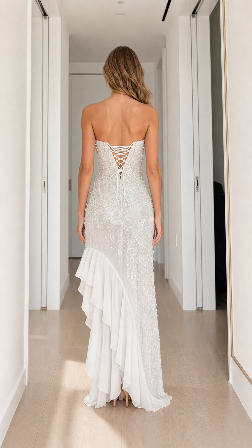 Back view of white strapless evening gown showing corset lace-up closure and ruffled train