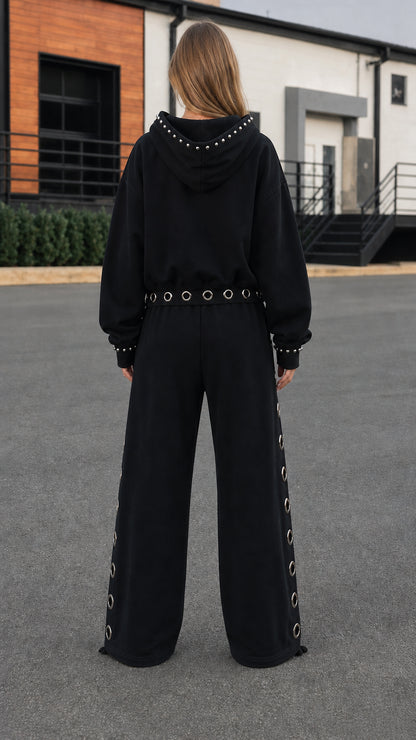 Back view of model wearing black hoodie with studded trim and wide-leg sweatpants