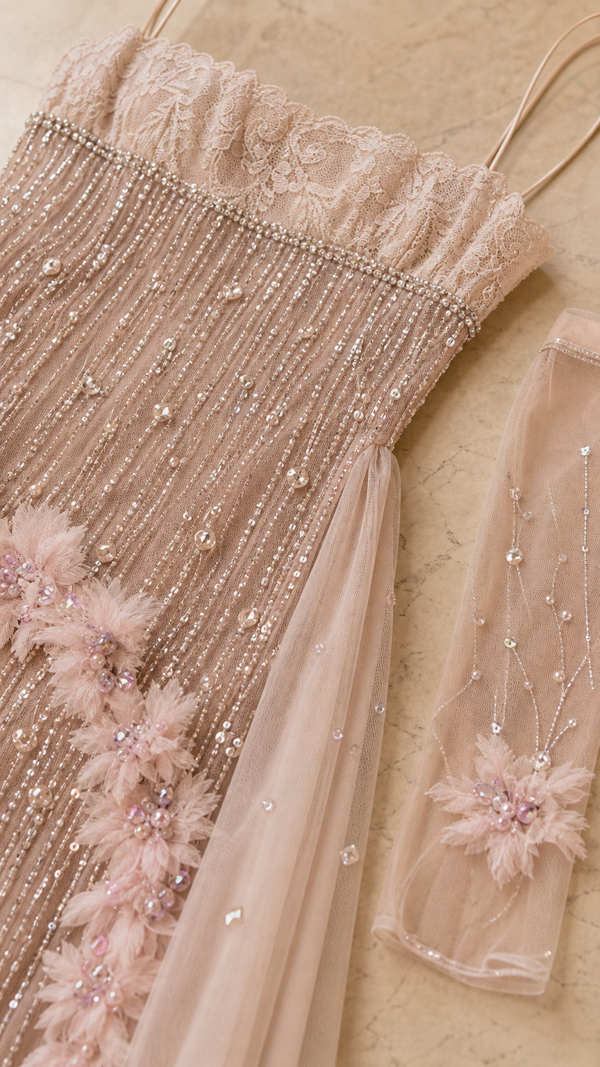 Close-up of blush gown beadwork, lace-like bodice detail, floral appliqué, and sheer sleeve accessory