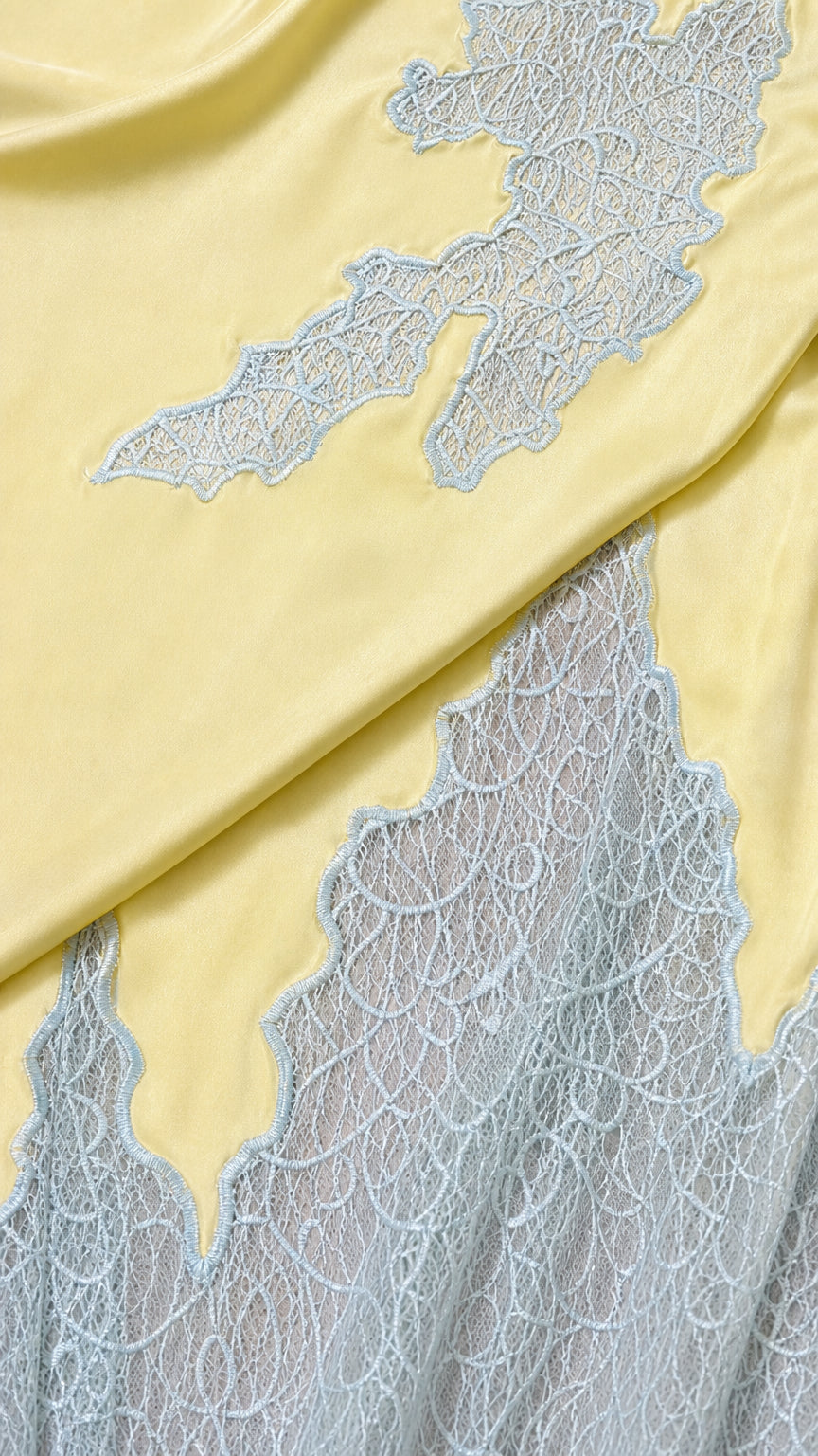 Close-up detail of yellow satin fabric and delicate light blue floral lace embroidery