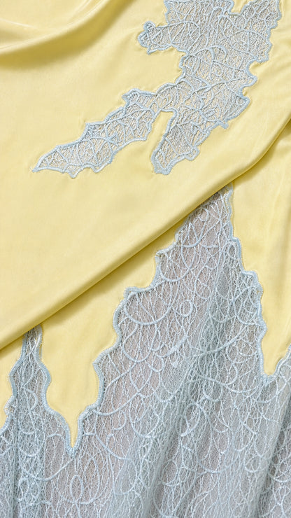 Close-up detail of yellow satin fabric and delicate light blue floral lace embroidery