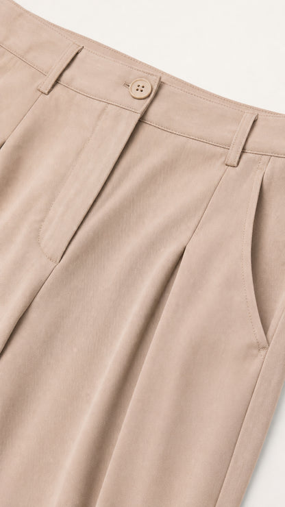 Close-up detail of beige trouser waistband, button closure, belt loops, and front pleating