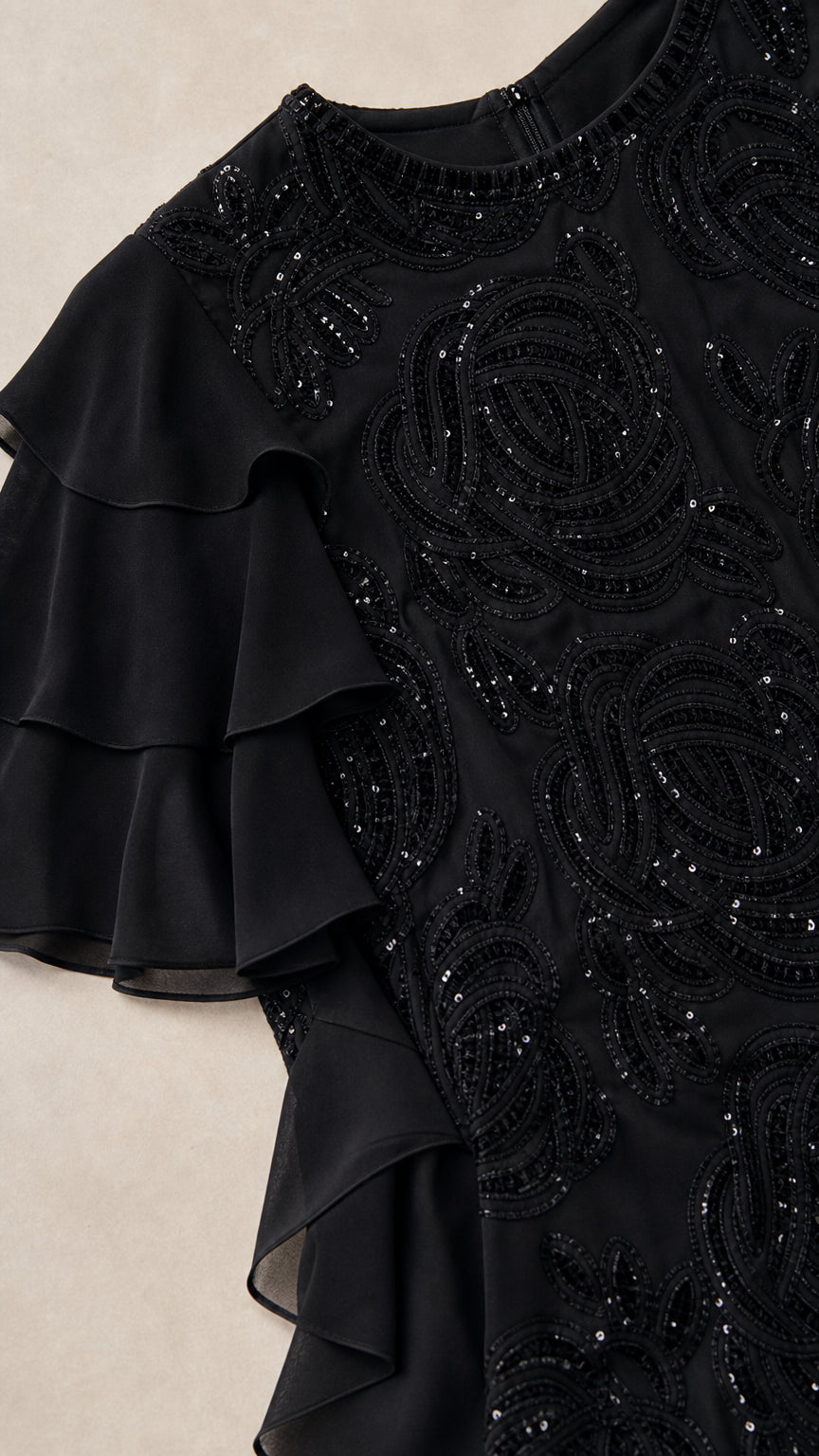 Close-up detail of black dress beadwork and ruffle sleeve